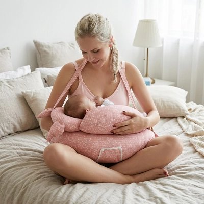 Coussin allaitement rose blanc bébé dort dans les bras de maman assis sur lit